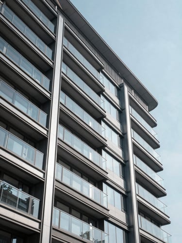 Crisp, high-contrast daylight shot of a modern real estate development facade, steel and glass structure reflecting clear sky.