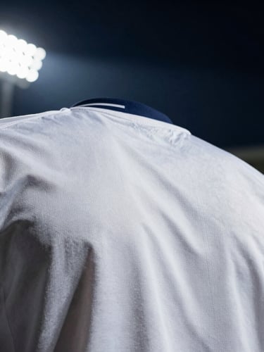 Cinematic close-up of the pristine white fabric of a classic football shirt, high-contrast stadium floodlights casting dramatic shadows on the texture, minimalist composition, 35mm lens.