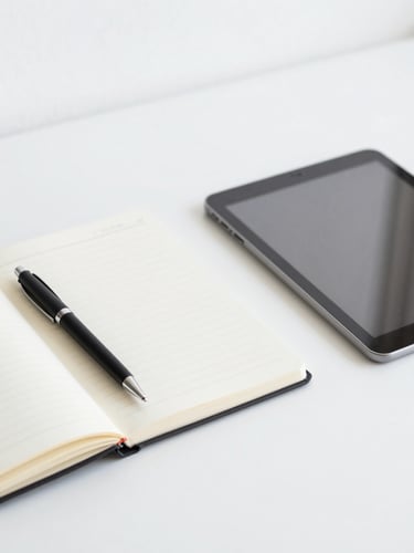 Minimalist close-up of an organized remote workspace desk with a notebook, pen, and clean tablet under bright neutral daylight.