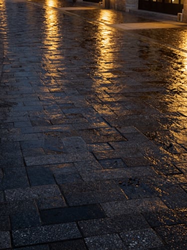 Manicured luxury resort pathway with heavy-duty Kandla Grey cobblestones, wet finish reflecting warm golden landscape lights, high-contrast night shot