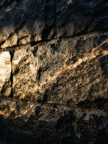 Low-key architectural photography of raw dark stone slabs with dramatic golden side lighting, highlighting deep charcoal textures and warm champagne veining, 35mm.