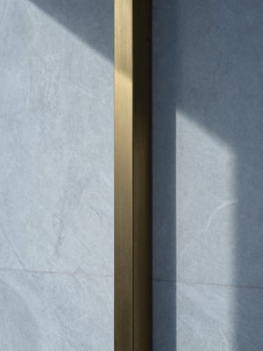 Extreme close-up of a polished white Swiss quartzite wall meeting a brushed brass column, sharp geometric shadow lines, cool overcast morning light, 35mm.