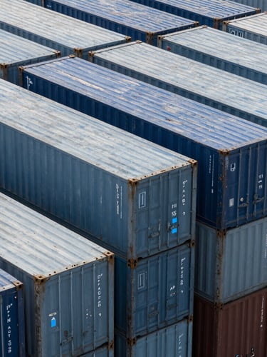 High-angle structured pattern of modern deep-water port container stacks under cool crisp daylight, subtle blue tech glows on metal edges, sharp 35mm architectural lens.