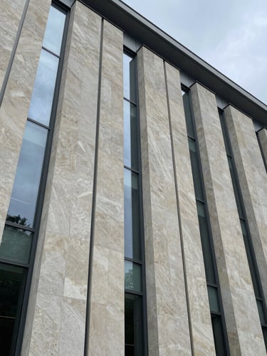 Extreme wide-angle architectural composition of a limestone facade under overcast daylight, clean vertical glass lines, minimalist structural steel.