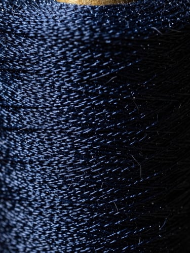 Extreme close-up, macro lens view of a spool of deep navy, high-resistance embroidery thread, with dramatic side-lighting emphasizing its texture and strength.
