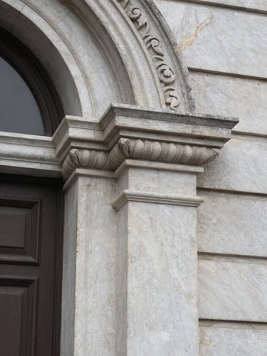 Close-up of a marble building detail — carved stone molding at a palazzo entrance in northern Italy, overcast flat light, fine grain texture of the stone visible, no people, tight architectural crop