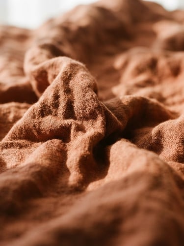 Tight macro shot of rumpled terracotta linen fabric, soft afternoon window light, high-contrast shadows highlighting the rich tactile weave, shallow depth of field, 35mm