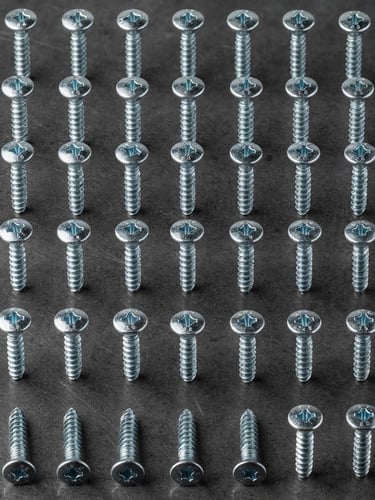 Macro shot of organized zinc-plated steel screws on a clean dark gray metal background, crisp studio light, industrial precision framing