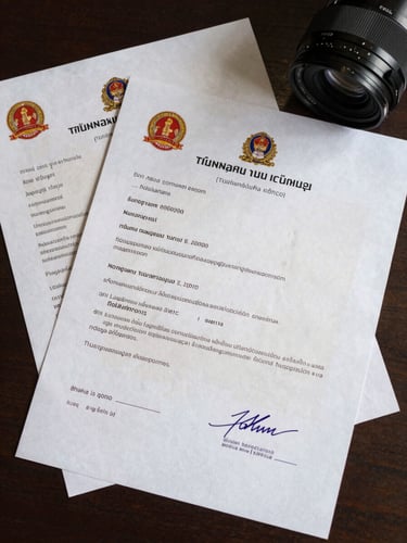 Close overhead shot of official Thai film permit documents spread on a desk, government stamps and signatures visible, even studio lighting, no faces