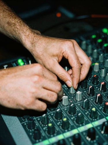 Close-up of hands adjusting dials on an analog mixing console in a dark studio, neon green backlighting, high contrast 35mm flash photography.