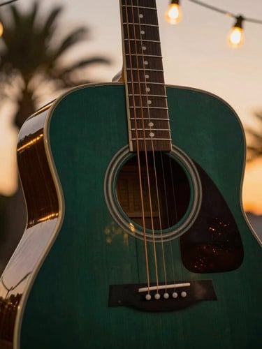Tight shallow-depth-of-field shot of an acoustic guitar body under warm incandescent string lights, rich deep green and amber tones, palm tree silhouettes in the background.