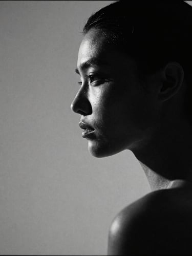 High-fashion model portrait in sharp profile, dramatic studio lighting with deep shadows, stark black and white, 35mm film grain, negative space on the left