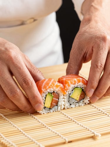 Close-up of a chef's hands carefully rolling a sushi roll with fresh avocado and salmon, clean bamboo mat, warm directional studio light, premium feel