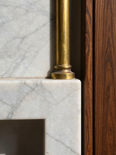 Portrait framing, extreme close-up detail of honed Arabescato marble meeting patinated unlacquered brass and deep walnut wood, sharp authentic shadows from natural daylight, highlighting precise material intersections.