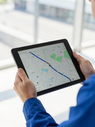 A close-up of a technician's hand holding a digital tablet displaying a live map route, bright daylight, sharp focus, crisp blue uniform sleeve visible.