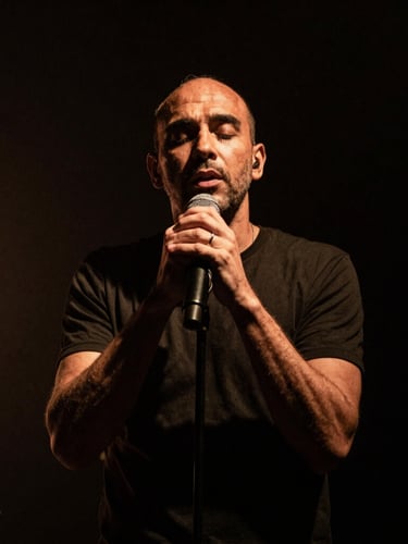Dramatic stage lighting on Pierre-Yves Clarence performing live, low-key photography, deep shadows, high contrast, warm amber undertones, vertical portrait crop