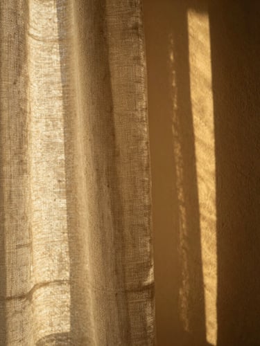 Macro photograph of heavy oatmeal linen curtain casting deep, high-contrast shadows on a warm plaster wall, strong golden hour sunlight, 35mm editorial style