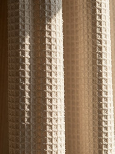 Macro shot of heavy waffle-weave shower curtain fabric in oatmeal, strong directional morning sunlight casting deep shadows across the deep ridges