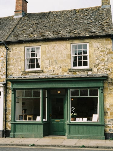 Warm editorial photography of a traditional wooden shopfront in a UK village, muted green tones, soft daylight, 35mm film.