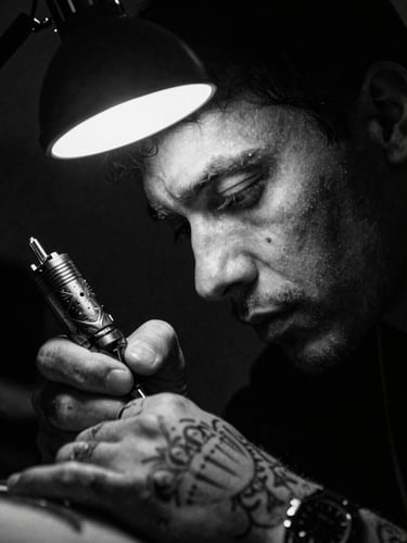 Extreme close-up of a tattoo artist focusing intensely under a sharp directional studio lamp, high-contrast black and white, dramatic chiaroscuro lighting, 35mm film grain