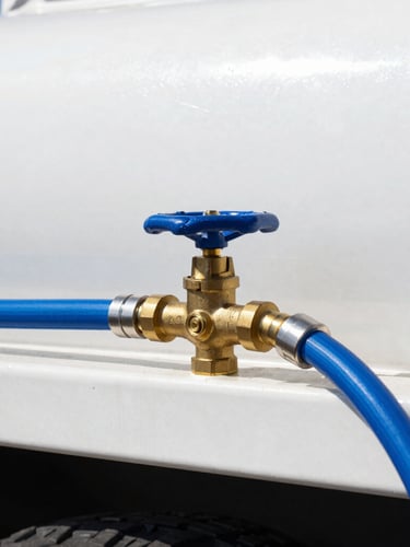 Close-up of a high-pressure brass valve on a clean white water truck, heavy-duty blue hose connected, bright midday Mexican sun, sharp focus
