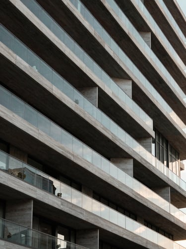 Vista arquitectónica abstracta de un edificio residencial moderno de hormigón y vidrio en Madrid, líneas geométricas limpias, luz natural difusa de la mañana, encuadre simétrico de ángulo contrapicado.
