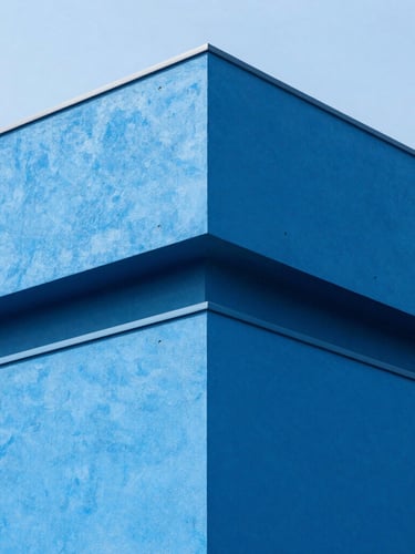 Sharp architectural corner of a modern concrete building painted in clean electric blue, high-key natural daylight, deep shadows, 35mm lens