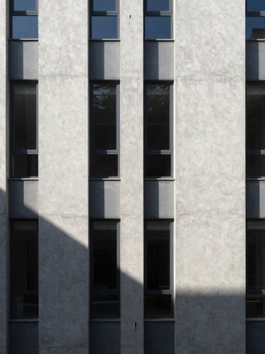 Vertical architectural crop of a minimalist concrete facade under harsh daylight, deep geometric shadows, 35mm lens.