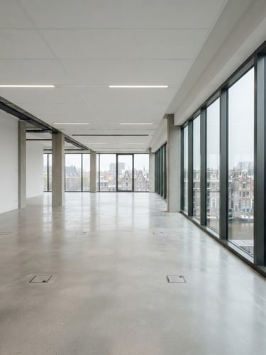 A wide-angle shot of a spacious, completely cleared modern office building in Amsterdam. Clean concrete floors, empty white walls, large windows letting in soft natural overcast light, pristine space ready for key handover.