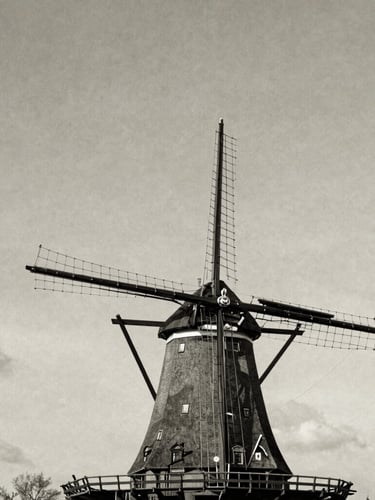 Historic black and white photograph of Molen De Lelie in the Dutch landscape, majestic sails angled against a soft textured sky, vintage editorial style