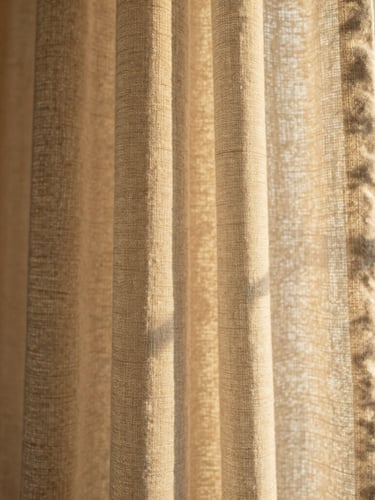 A cropped macro shot of draped oatmeal-colored linen curtains catching golden-hour window light, highlighting the rich tactile weave and soft morning side-light, 35mm photography