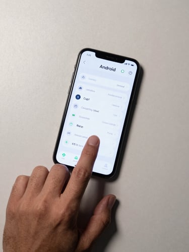 Overhead flat-lay close-up of a single hand resting on an Android phone face-up on a pale desk, one finger mid-tap on a clean minimal UI, clean studio light from upper left, muted tones