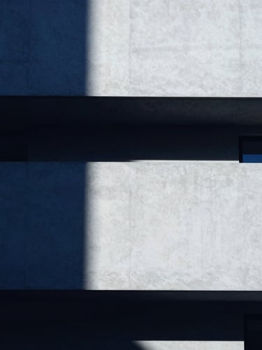 Minimalist architectural crop of a modern concrete building facade, sharp high-contrast studio light, deep indigo shadows, clean lines, 35mm lens