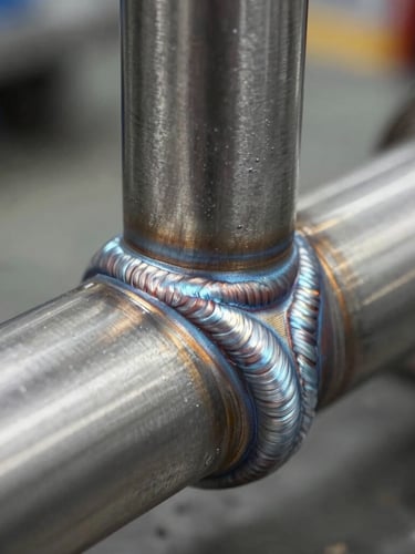 Close-up macro of a flawless TIG weld on a stainless steel pipe joint, cold metallic silver tones, clean industrial workshop setting, sharp focus on the weld pattern