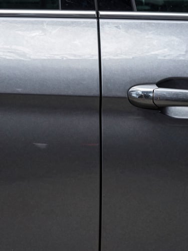 Extreme close-up of a car door panel, left half showing a sharp dent crease in dark metallic paint, right half showing the same surface perfectly restored — photographed straight-on under bright diffused studio strobes, no shadows, clinical documentation framing