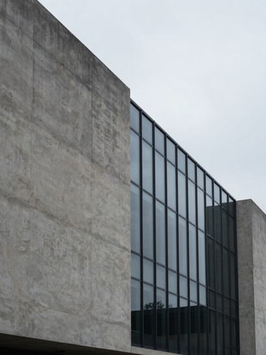 Minimalist concrete and glass architectural facade, sharp angles, soft overcast daylight, generous negative space on the left, high-contrast shadows.