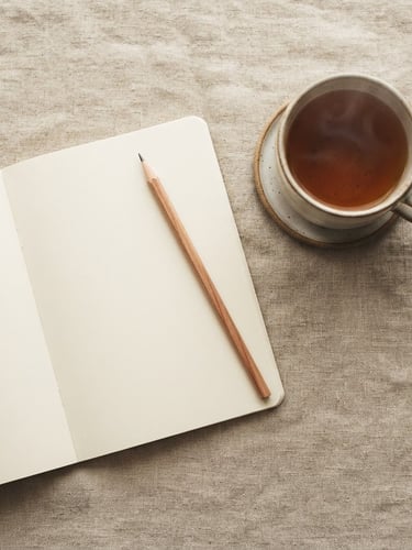 An overhead flat-lay of a minimalist notebook, a wooden pencil, and a warm cup of tea on a textured linen surface, soft morning daylight, shallow depth of field.