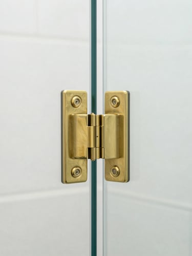 Crisp architectural close-up of heavy-duty solid brass hinges on a frameless glass shower door, bright high-key natural daylight, clean reflections, sharp focus, 35mm lens