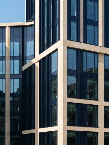 Architectural detail of a modern stone and glass financial building facade, sharp focus, bright natural daylight, deep navy and warm cream tones.