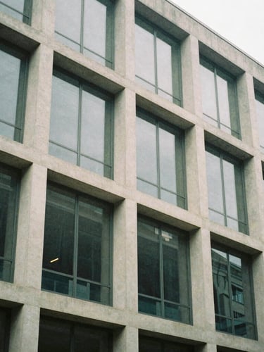 Abstract structural geometry of a mid-century modern office building facade, concrete and glass panels, soft overcast daylight, muted tones