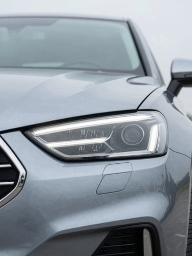 Close-up of a clean, modern sports sedan headlight and metallic grille, soft overcast daylight, cool slate metallic tones, sharp focus, 50mm lens