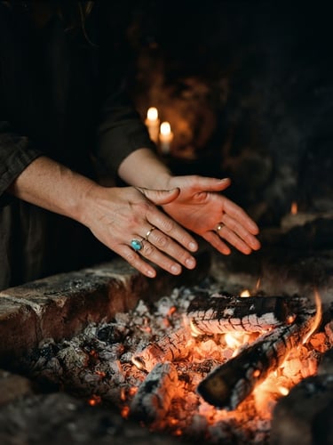 Moody editorial photography, close-up of hands hovering in a healing gesture over warm glowing embers, low-key candlelight, deep shadows, 35mm