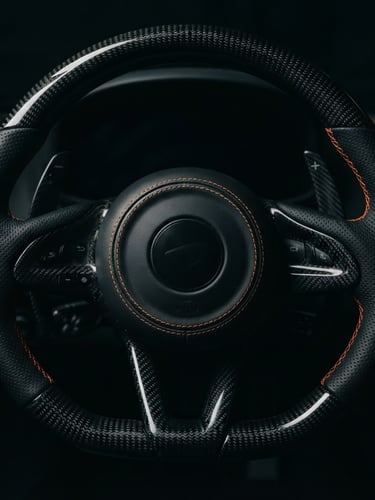 Moody close-up of a sports car steering wheel with carbon fiber details, low-key dramatic lighting, sharp orange stitching highlights, 50mm lens