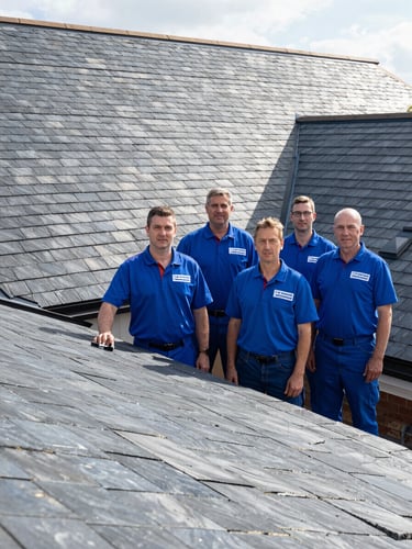 A clean team of professional British roofers in matching branded blue uniforms standing in front of a newly completed slate roof, bright natural daylight, sharp architectural photography, wide-angle lens, high-contrast slate and blue tones.