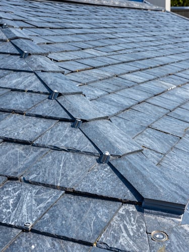 Crisp close-up photograph of precise lead work and dry verge systems on a newly completed slate roof, bright daylight, high-contrast blue and slate tones