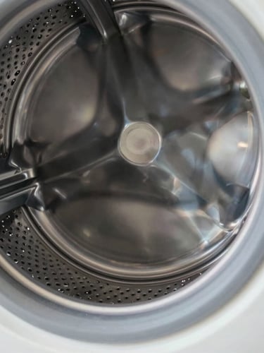 Macro close-up of a clean stainless steel washing machine drum, bright natural light reflecting off the metallic texture, sharp focus on the precision-milled drain holes, technical and clean.