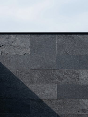 Minimalist architectural detail of a modern stone facade with sharp shadows, soft diffused overcast daylight, muted slate tones, medium format.