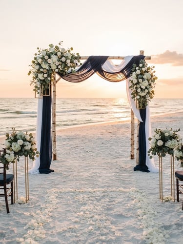A pristine beach wedding setup at sunset on Madeira Beach, Florida. An elegant wooden arch draped in deep navy blue and crisp white linens with subtle gold floral stands. The Gulf of Mexico waves gently lapping in the background, warm golden-hour light casting long soft shadows on the clean white sand.