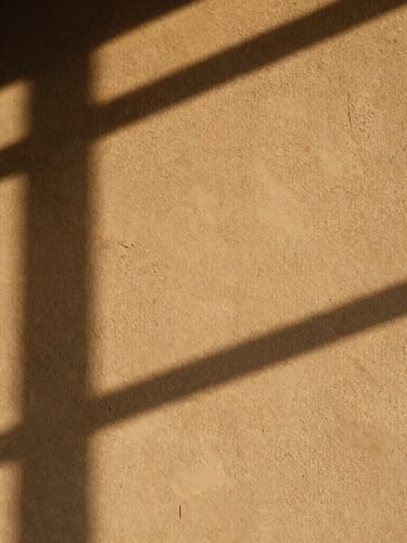 Warm raw plaster wall catching low-angle afternoon sunlight, soft long shadows, tactile texture, minimal composition, 35mm photography