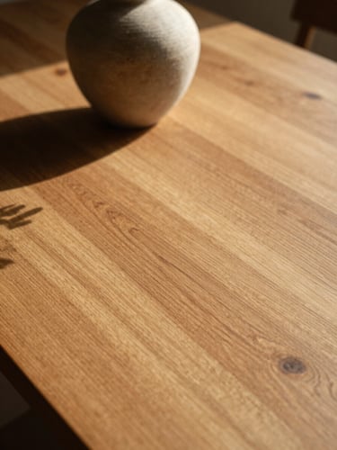 Close-up of a sun-drenched solid oak dining table, warm low-angle afternoon sunlight casting long shadows of a stoneware vase, 35mm editorial photography.